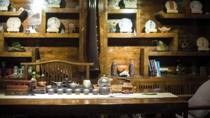 A wooden shelf with clocks and a table with tea sets and a small model train. - ‌The Secret Garden of Cats & Wolf's Den Barista Courtyard Cafe & Inn (Wuyi Street) (Lijiang)