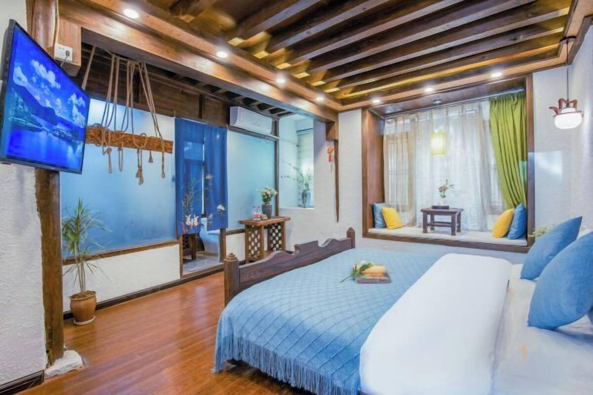 A bedroom with a bed, a TV, a window with curtains, and a wooden ceiling.