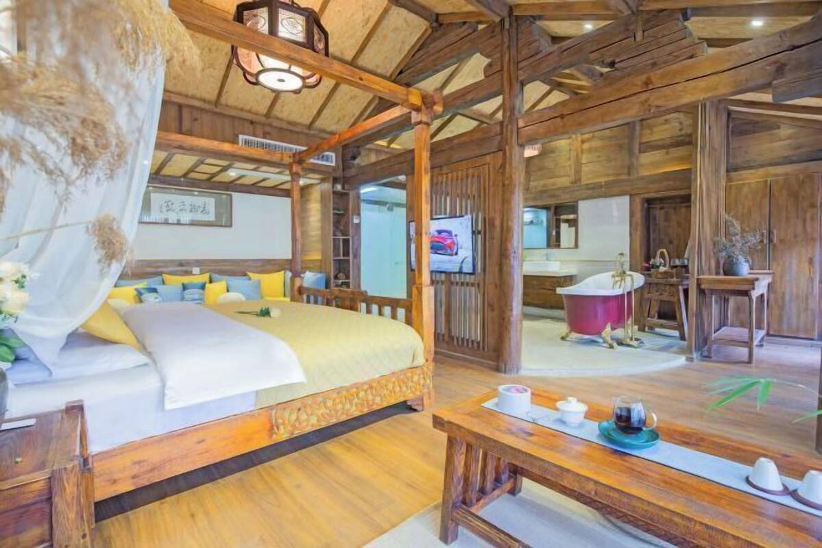 A traditional wooden room with a bed, a table with tea set, and a red bathtub.