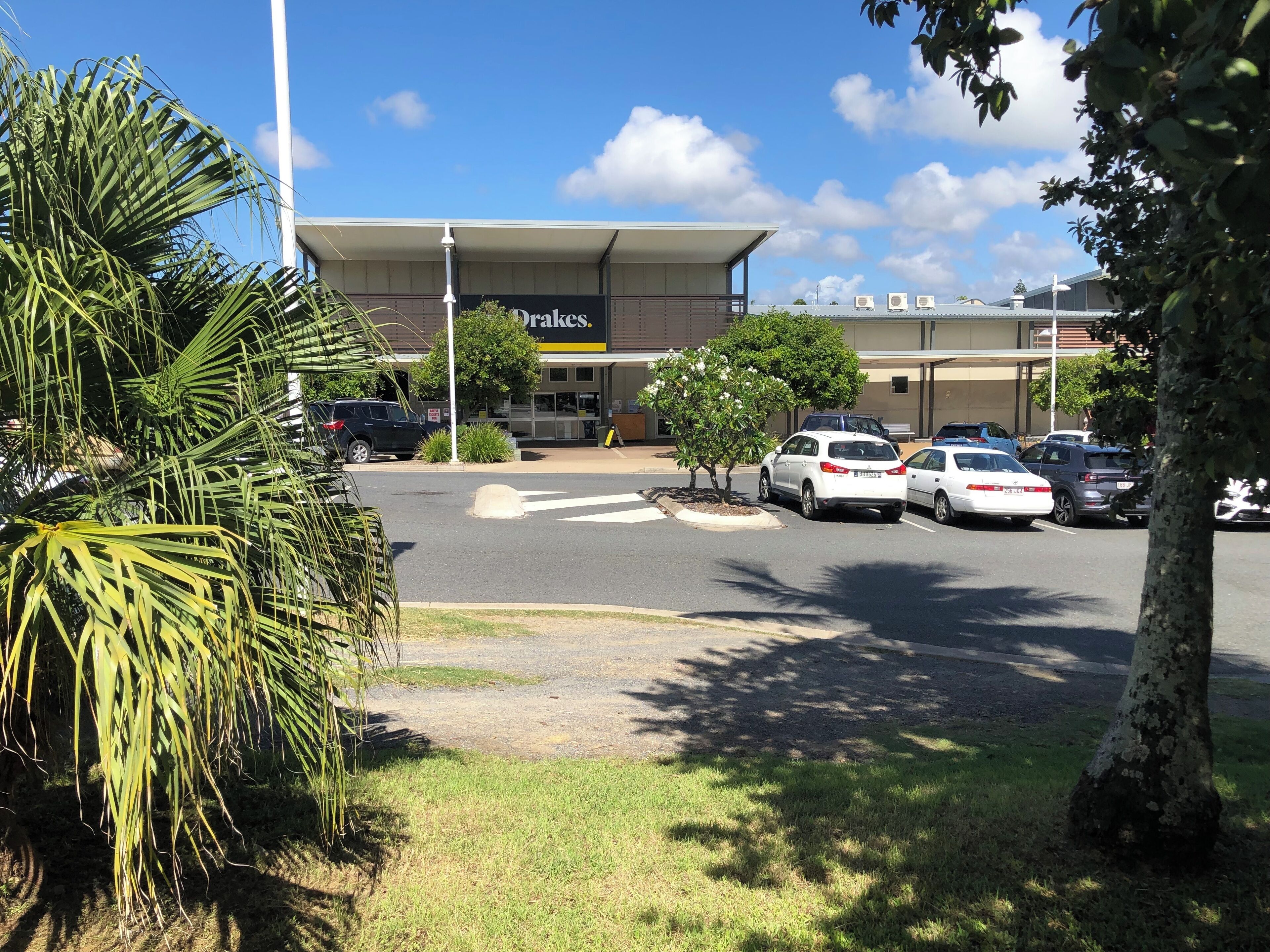 A parking lot with several cars, a building with a sign reading 'Oakes,' and surrounding greenery.