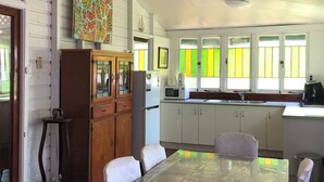 A dining area with a table and chairs, a kitchen with cabinets and a refrigerator, and a window with a view of greenery.