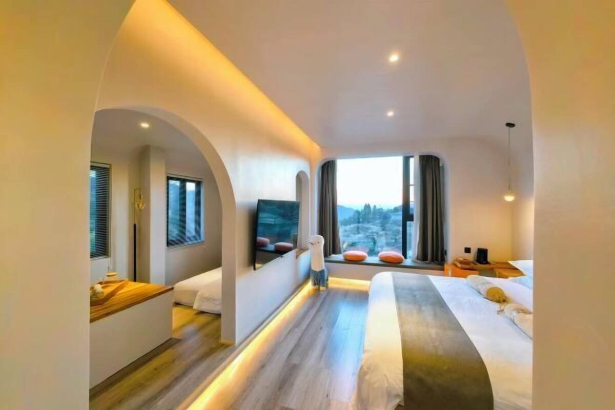 Quarto de hotel moderno com uma cama grande, televisão, escrivaninha e vista para o exterior.