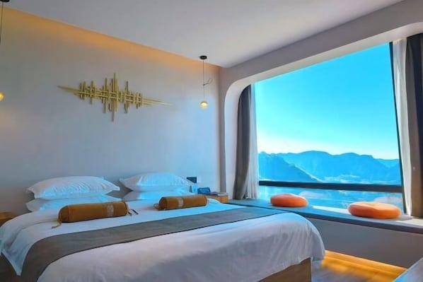 Habitación de hotel moderna con una cama grande, un adorno en la pared y vistas a las montañas a través de un ventanal amplio.