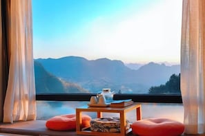 Una habitación con vistas a las montañas, una mesita con una tetera y dos cojines rojos.