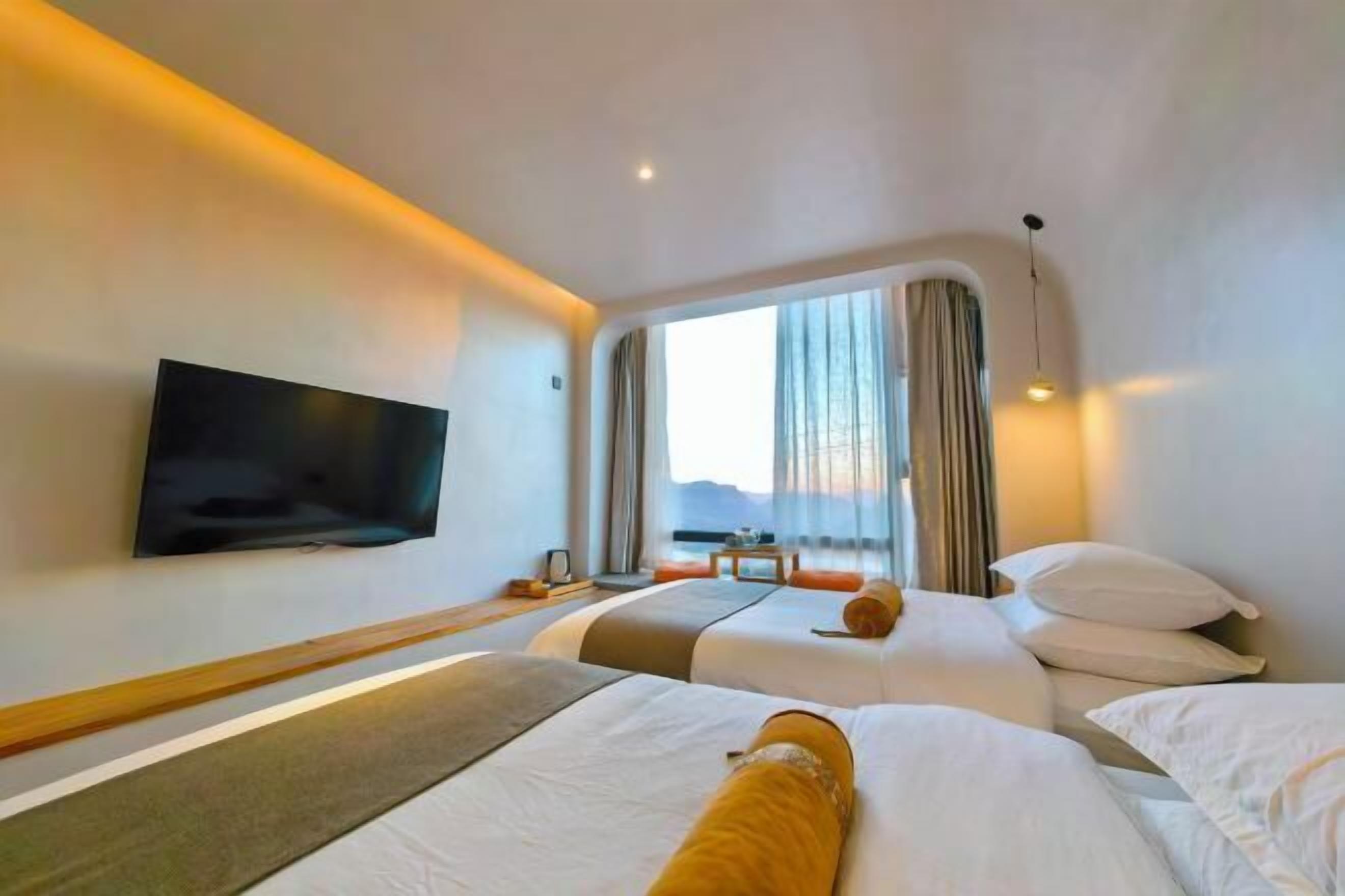 A hotel room with two beds, a TV, a window with curtains, and a view of the sea.