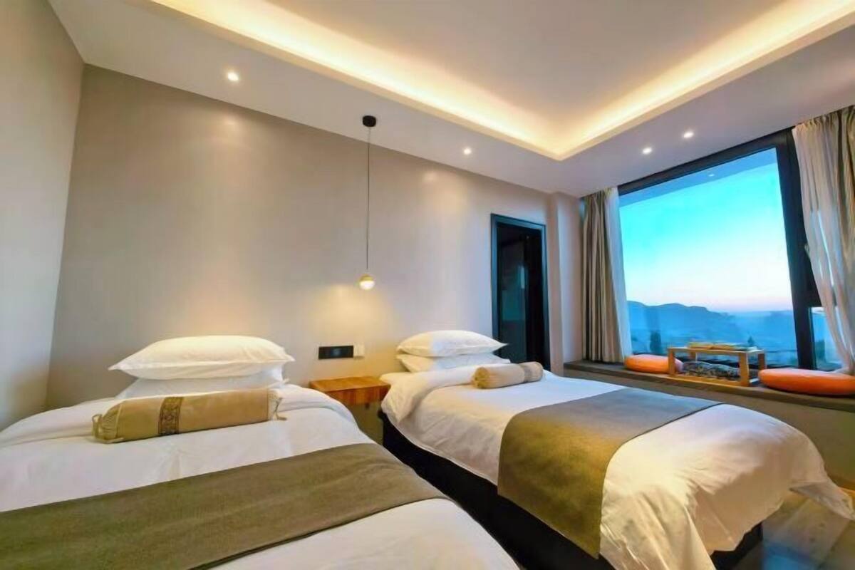 Quarto de hotel com duas camas, uma janela ampla com vista e um lustre.