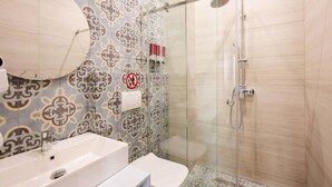 Casa de banho com azulejos estampados, lavatório, sanita e cabine de duche com vedação de vidro.