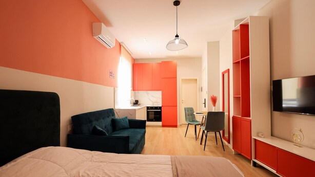 A modern hotel room with a large bed, a seating area with a sofa and chairs, a TV, and a kitchenette in the background. - Heart of Durres Apartment 02 (Durrës)