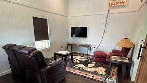 A living room with a leather recliner, a red armchair, a small table, a TV mounted on the wall, and a star-patterned rug.