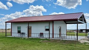 A single-story metal building with a red roof, two doors, and a covered porch area with a bench.