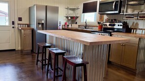 A kitchen with a large island, bar stools, stainless steel appliances, and wooden cabinetry.