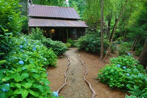Eine rustikale Holzhütte mit einer hölzernen Veranda, umgeben von üppigem Grün und einem Kiesweg.