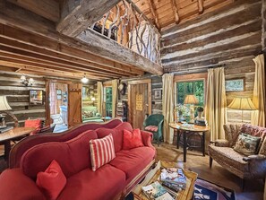 Ein Holzblockhaus-Innenraum mit einem roten Sofa, einem Holzesstisch und Blick durch ein Fenster.