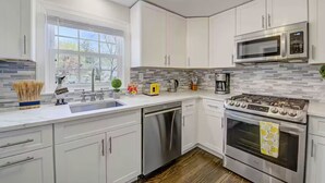 Une cuisine moderne avec des meubles blancs, un lave-vaisselle en acier inoxydable, une cuisinière à gaz et un four à micro-ondes.