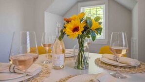 Une table à manger dressée avec des verres à vin, une bouteille de vin et un vase rempli de tournesols.
