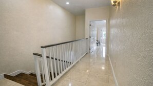 A hallway with a white railing, a door at the end, and a light fixture on the wall. - Entire Private 2BR 2 Bath Townhouse Near Seven Mile Beach w/ Balcony + Garden (George Town)