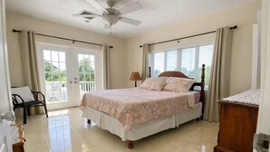 A bedroom with a bed, a chair, a desk, a ceiling fan, and a window with curtains. - Entire Private 2BR 2 Bath Townhouse Near Seven Mile Beach w/ Balcony + Garden (George Town)