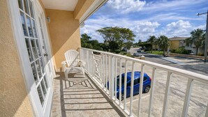 A balcony with a white chair, a blue car parked outside, and a clear sky. - Entire Private 2BR 2 Bath Townhouse Near Seven Mile Beach w/ Balcony + Garden (George Town)