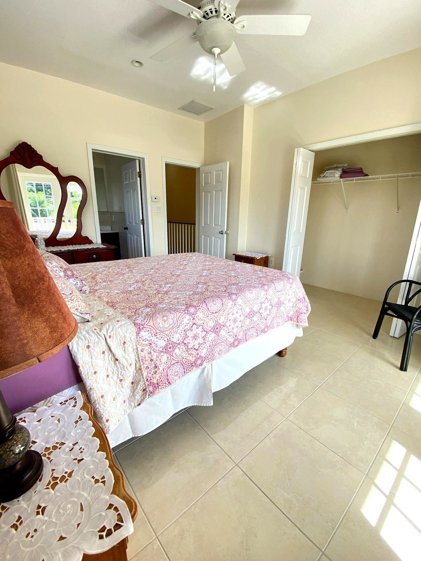 Une chambre à coucher comprenant un lit, un ventilateur de plafond, une armoire et une porte donnant sur une autre pièce.