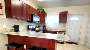 A kitchen with a central island, bar stools, a microwave, a coffee maker, and a window with blinds. - Entire Private 2BR 2 Bath Townhouse Near Seven Mile Beach w/ Balcony + Garden (George Town)