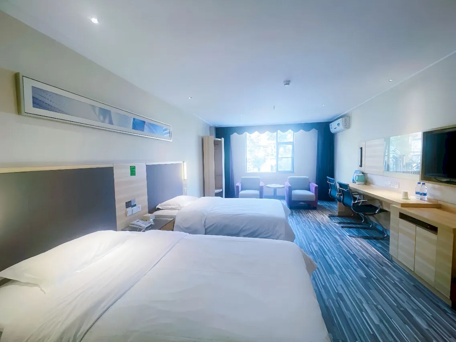 Une chambre d’hôtel avec deux lits, un bureau, une chaise, une télévision et une fenêtre.
