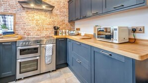 A kitchen with a brick wall, stainless steel appliances, and dark blue cabinets. - Cozy Countryside Cottage Retreat in Elkesley (Retford)
