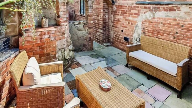 A patio area with wicker furniture, a stone table, and a brick wall. - Cozy Countryside Cottage Retreat in Elkesley (Retford)