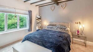 A bedroom with a bed, a bedside table, a window, and a ceiling with exposed beams. - Cozy Countryside Cottage Retreat in Elkesley (Retford)
