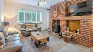 A living room with a brick fireplace, a sofa, a coffee table, and a television mounted above the fireplace. - Cozy Countryside Cottage Retreat in Elkesley (Retford)