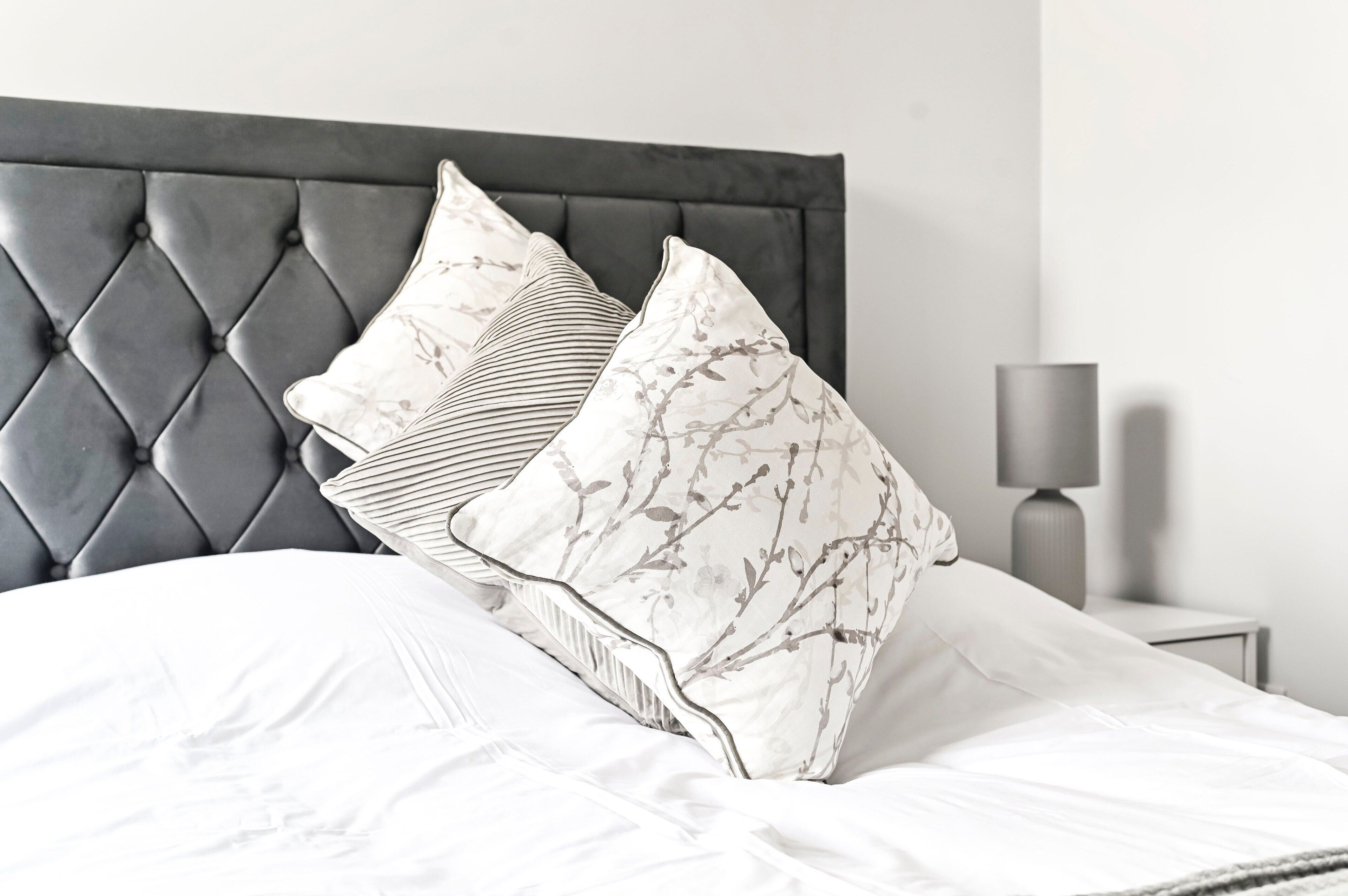 A bed with a tufted headboard, white bedding, and decorative pillows.
