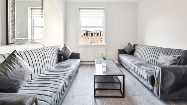 Un salon moderne avec deux canapés gris, une table basse en verre et un grand miroir au mur.
