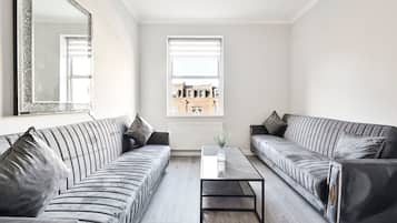 A modern living room with two grey sofas, a glass coffee table, and a large mirror on the wall.