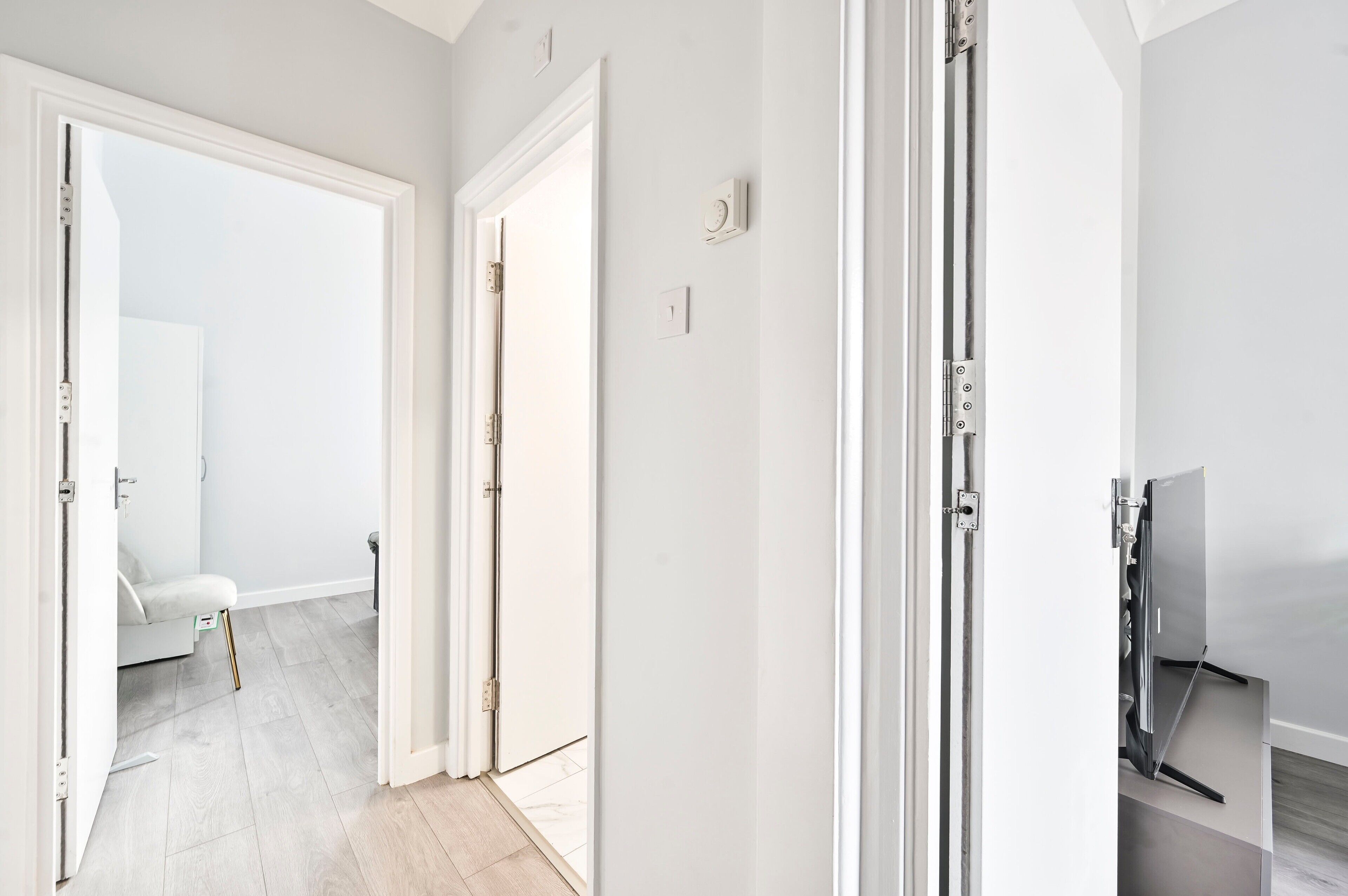 A hallway with white walls, a light-colored floor, and a door leading to another room.