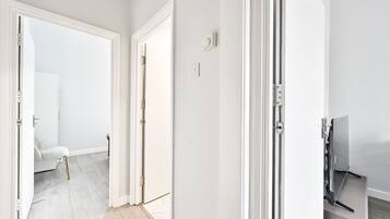 A hallway with white walls, a light-colored floor, and a door leading to another room.