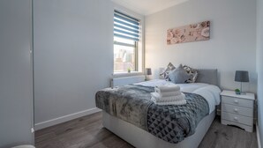 A modern bedroom with a large bed, a nightstand, a window with blinds, and a floral artwork on the wall. - Modern Flat in Waterloo - Central London (London)