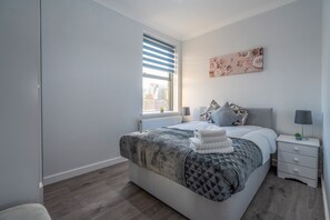 A modern bedroom with a large bed, a nightstand, a window with blinds, and a floral artwork on the wall. - Modern Flat in Waterloo - Central London (London)