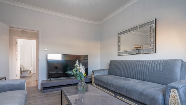 A modern living room with a grey sofa, a flat-screen TV, and a decorative mirror. - Modern Flat in Waterloo - Central London (London)