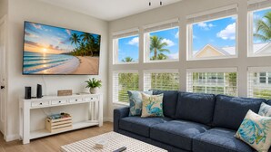 A living room with a large TV, a white console table, a blue sofa, and a view of the beach through large windows. - MG303l, Shared Heated Pool, Pet Friendly (Port Aransas)