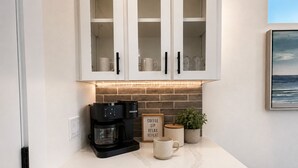 Et køkken med hvide skabe, kaffemaskine, et skilt med teksten 'COFFEE SIP RELAX REPEAT', en potteplante og en marmor bordplade.