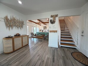 A spacious interior with a wooden staircase, a rattan console, and a kitchen area. - SS304 Private Pool, Charcoal Grill, Golf Cart Access (Port Aransas)
