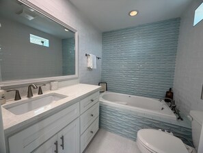 A bathroom with a large mirror, two sinks, a bathtub, and a toilet. - SS304 Private Pool, Charcoal Grill, Golf Cart Access (Port Aransas)
