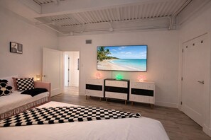 A bedroom with a bed, a checkered throw, a TV with a beach scene, and a console table with decorative lights. - SS304 Private Pool, Charcoal Grill, Golf Cart Access (Port Aransas)