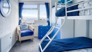 A bunk bed room with a view of the sea, a desk with a chair, and a sofa. - Seaward Apartment - 2 Bed Apartment - Saundersfoot (Saundersfoot)