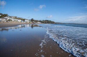 Ein Strand mit sandigem Ufer, ruhiger See und Gebäuden im Hintergrund.