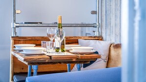 A wooden table with plates, glasses, and a bottle of wine, set against a rustic wall with metal pipes. - Seaward Apartment - 2 Bed Apartment - Saundersfoot (Saundersfoot)
