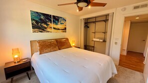 A bedroom with a bed, bedside lamps, a ceiling fan, a wardrobe, and a painting on the wall.