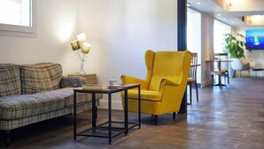 Een hal met een bank, een gele fauteuil, een tafel en een lamp.