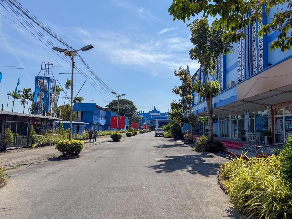 A street with buildings, a clear sky, and some greenery.