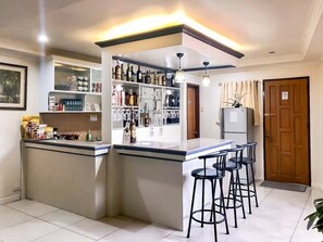 A kitchen with a bar area, bar stools, shelves with bottles, and a refrigerator.