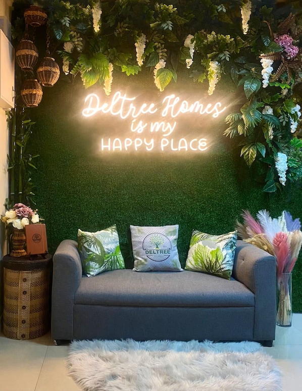 A cozy living area with a green wall, a neon sign, and a grey sofa with decorative pillows.